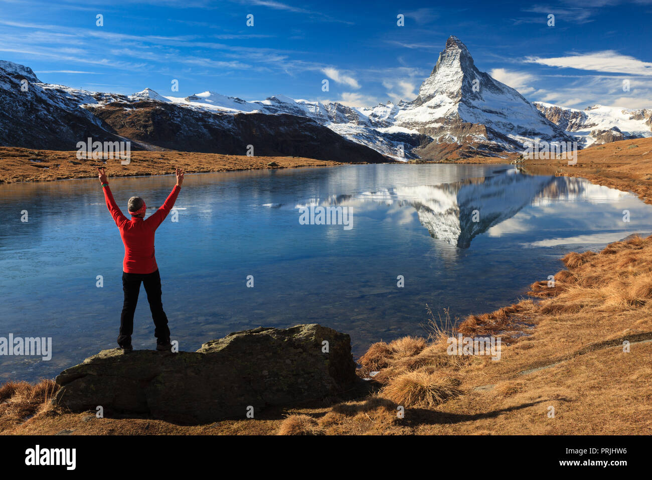 Eine Frau steht mit ihren ausgestreckten Armen auf einem Felsen, dahinter das Matterhorn ist in See Stelli, Zermatt wider Stockfoto