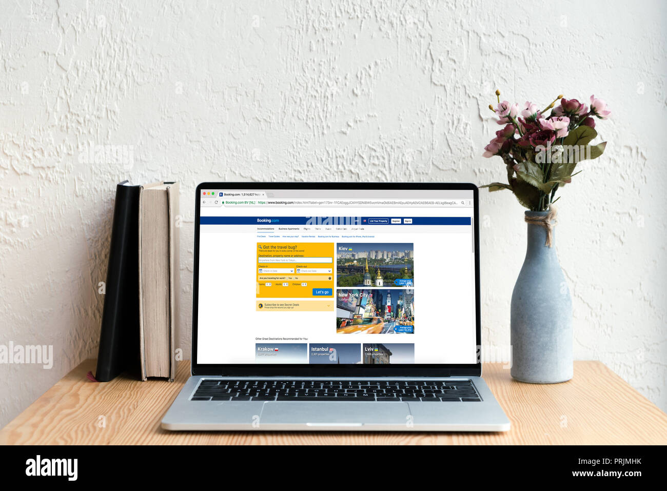 Laptop mit Webseite auf dem Bildschirm, Bücher und Blumen in Vase auf hölzernen Tisch Stockfoto
