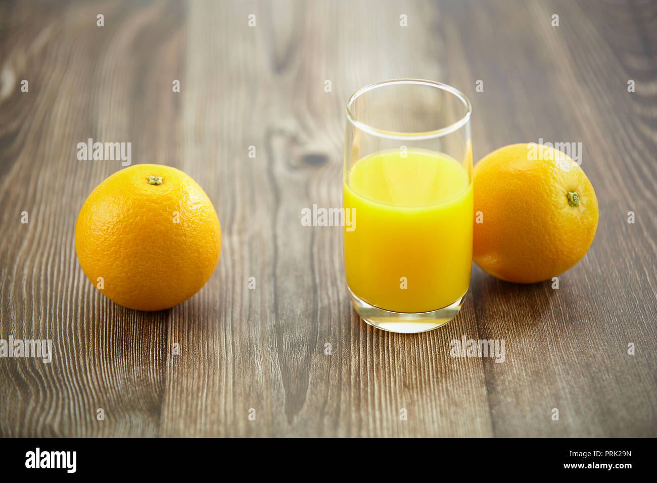 Zwei Orangen und ein Glas Orangensaft auf der Oberfläche des Holzes. Stockfoto