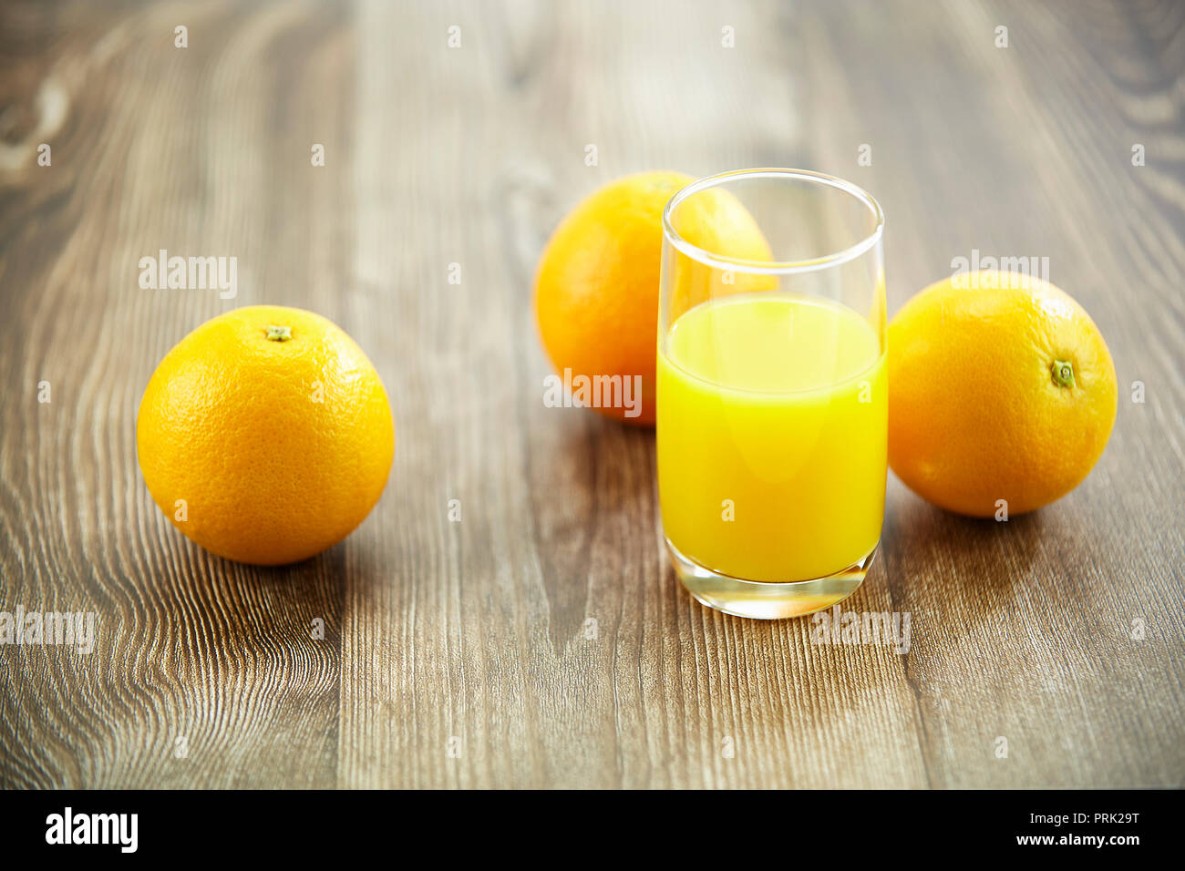 Drei Orangen und ein Glas Orangensaft auf der Oberfläche des Holzes. Stockfoto