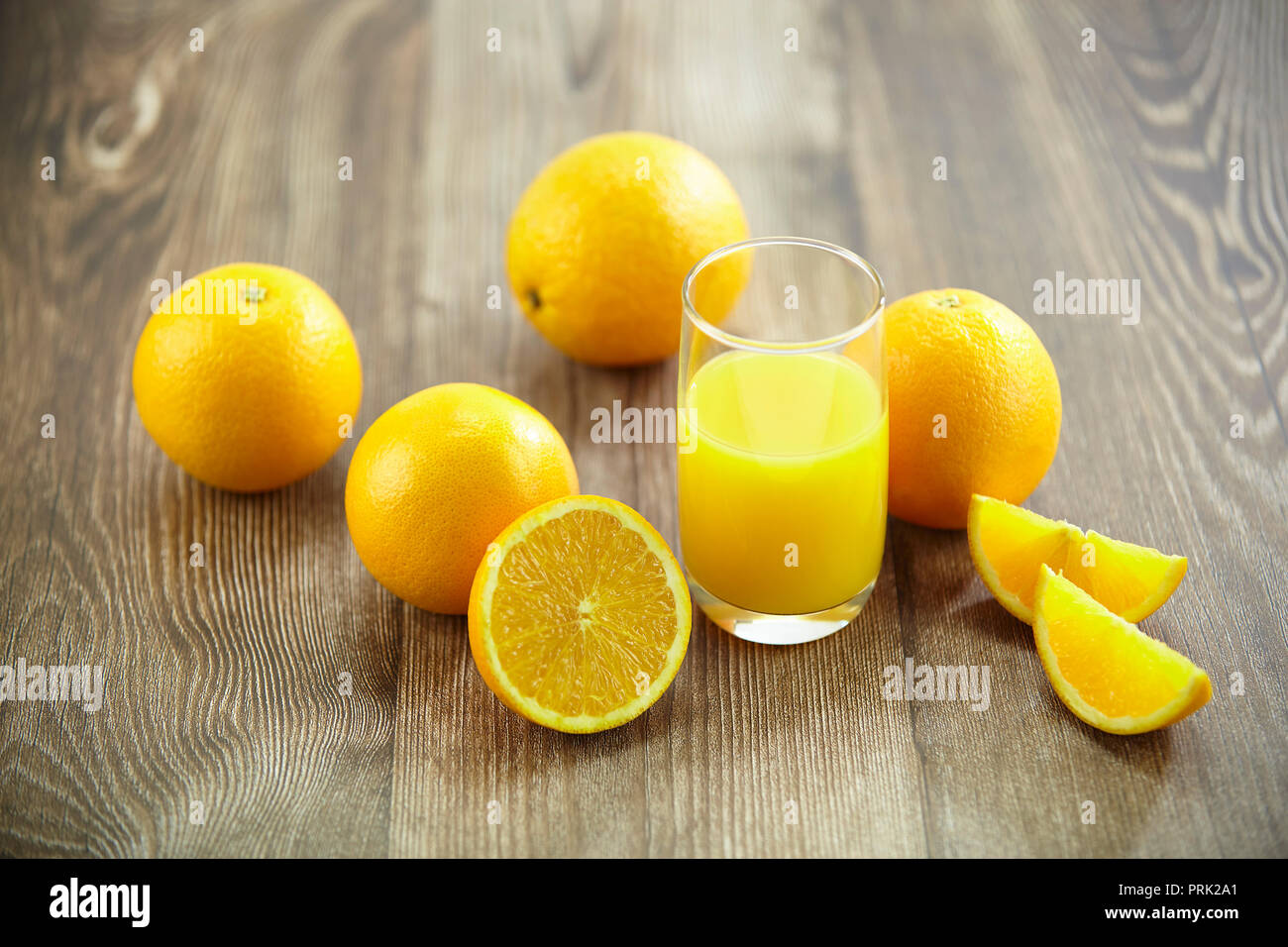 Mehrere Orangen und ein Glas Orangensaft auf der Oberfläche des Holzes. Stockfoto