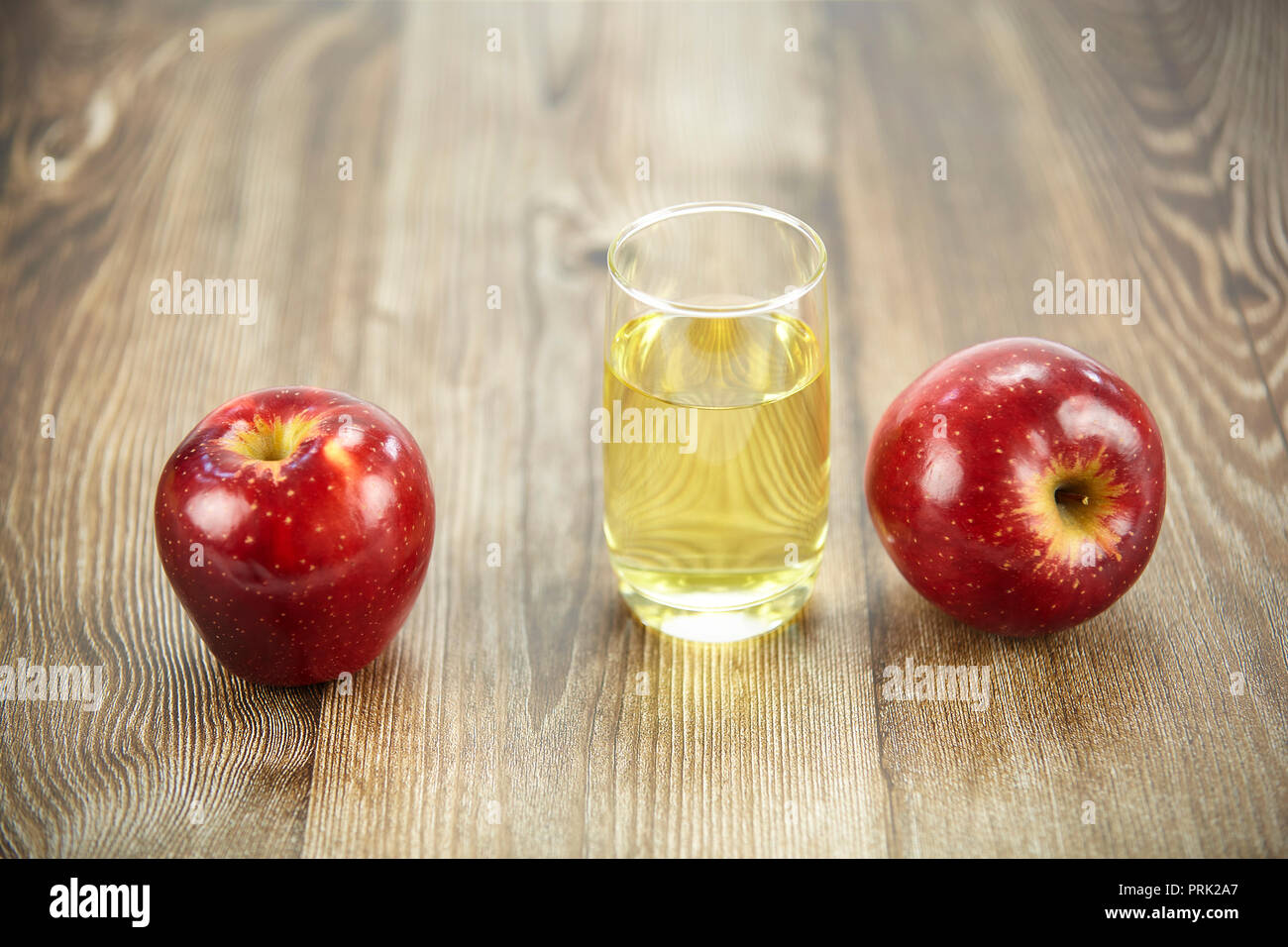 Zwei Äpfel und ein Glas Apfelsaft auf der Oberfläche des Holzes. Stockfoto