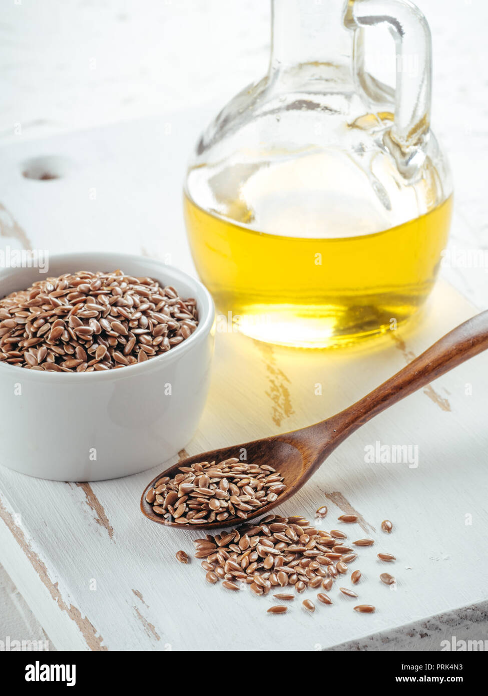 Brauner Leinsamen in Löffel und Leinsamenöl in Glasflasche auf weißem Holz- Hintergrund. Leinöl ist reich an Omega-3-Fettsäuren. Stockfoto