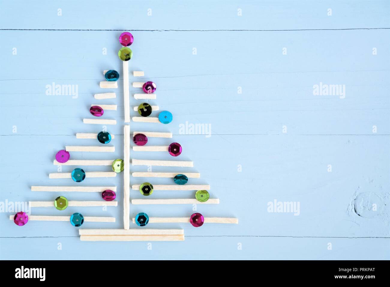 Weihnachtsbaum der kleinen Holzstäbchen und glänzenden Zierplättchen. Blau Holz- Hintergrund und Kopie Raum Stockfoto