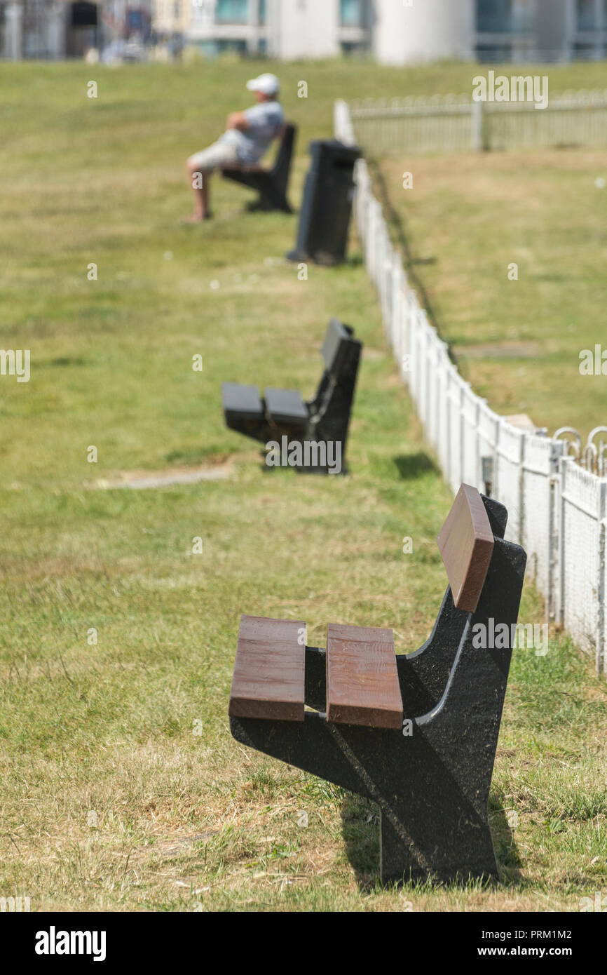 Sitzreihe bei Sonnenschein - vielleicht mit dem unsichtbaren Charakter, der ein Nickerchen macht. Für den Aufenthalt Cornwall Konzept, Covid Park Bank Wiederversammlungen. Stockfoto