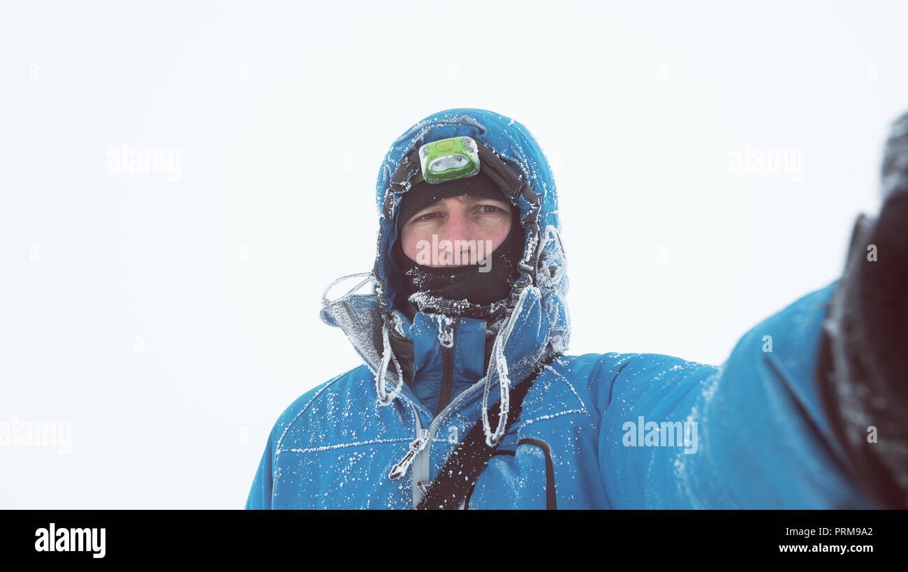 Europäische person Selfie portrait auf weißem Hintergrund. Raureif auf einer blauen Jacke. Frostigen Wintertag in dem trüben und kalten Wetter. Abenteuer tour Stockfoto