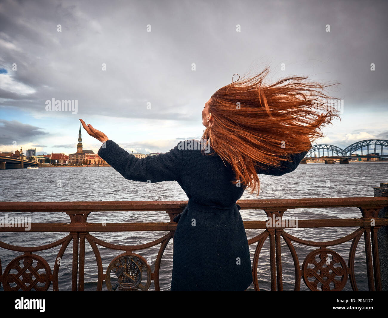 Ein junges Mädchen drehte sich Gesicht der Stadt ihre Hände angehoben. Ihr langes rotes Haar entwickelt sich in den Wind. Das Mädchen ist von hinten fotografiert. Stockfoto