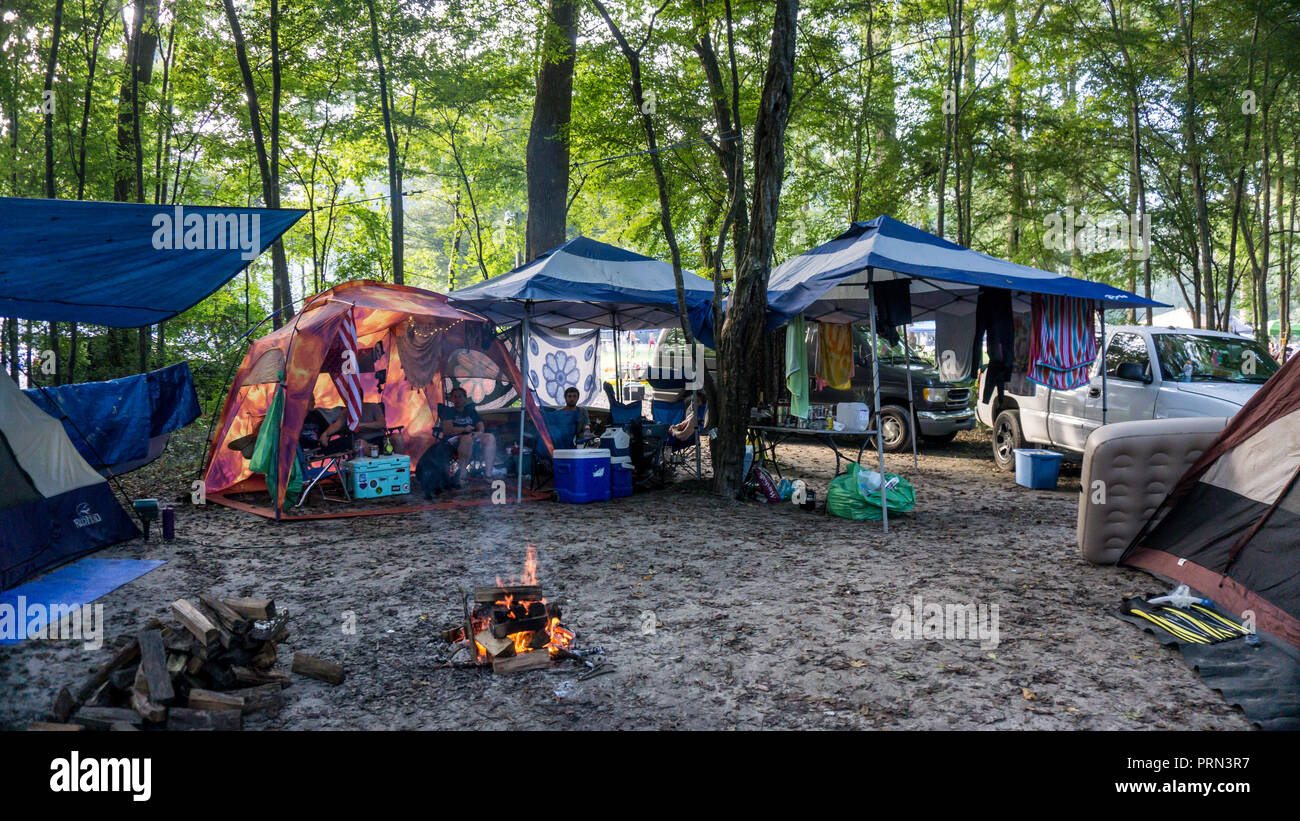 Menschen entspannen in einem bunten Lagerplatz rund um das Feuer mit Zelten, Transporter und Fahrzeuge im Wald in Ginnie Springs, Florida Stockfoto