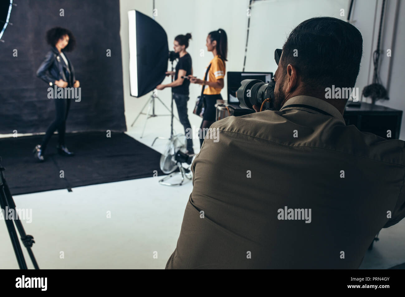 Weibliche Model posiert für Porträts auf schwarzem Hintergrund in einem Studio. Fotograf mit seiner Crew beim Fototermin im Studio. Stockfoto