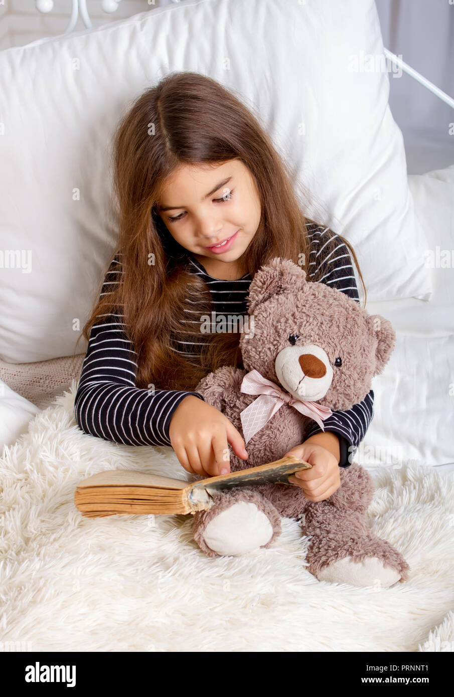 Kleines Mädchen auf dem Bett liegend mit ihren Teddybären und lesen Sie ein Buch vor dem Schlafengehen Stockfoto