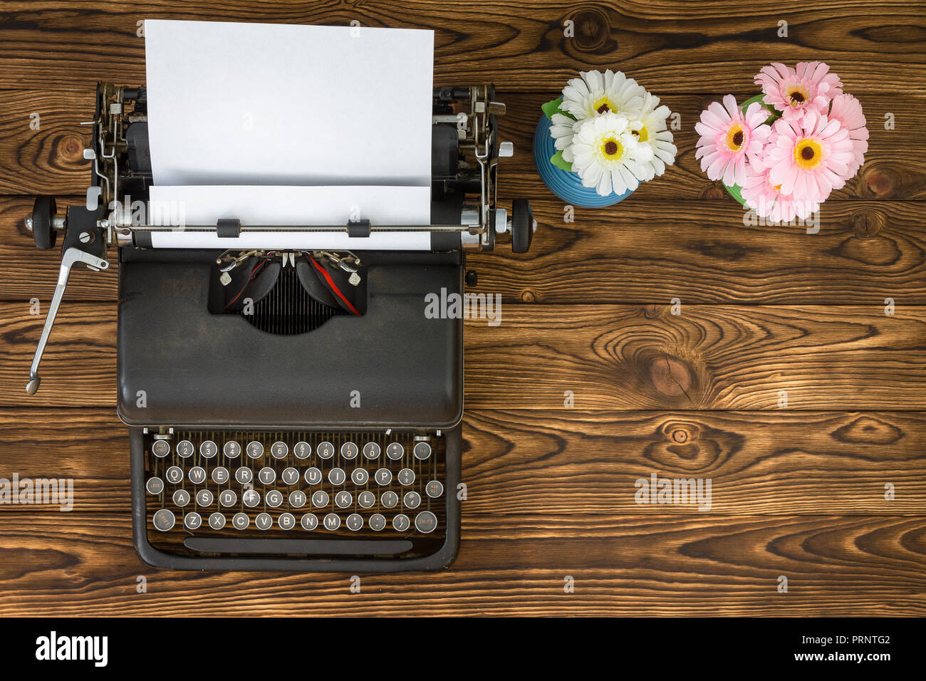 Ansicht von oben von Vintage metall Schreibmaschine neben blau und rosa Blüten sitzen auf Holzbrett Tabelle Stockfoto