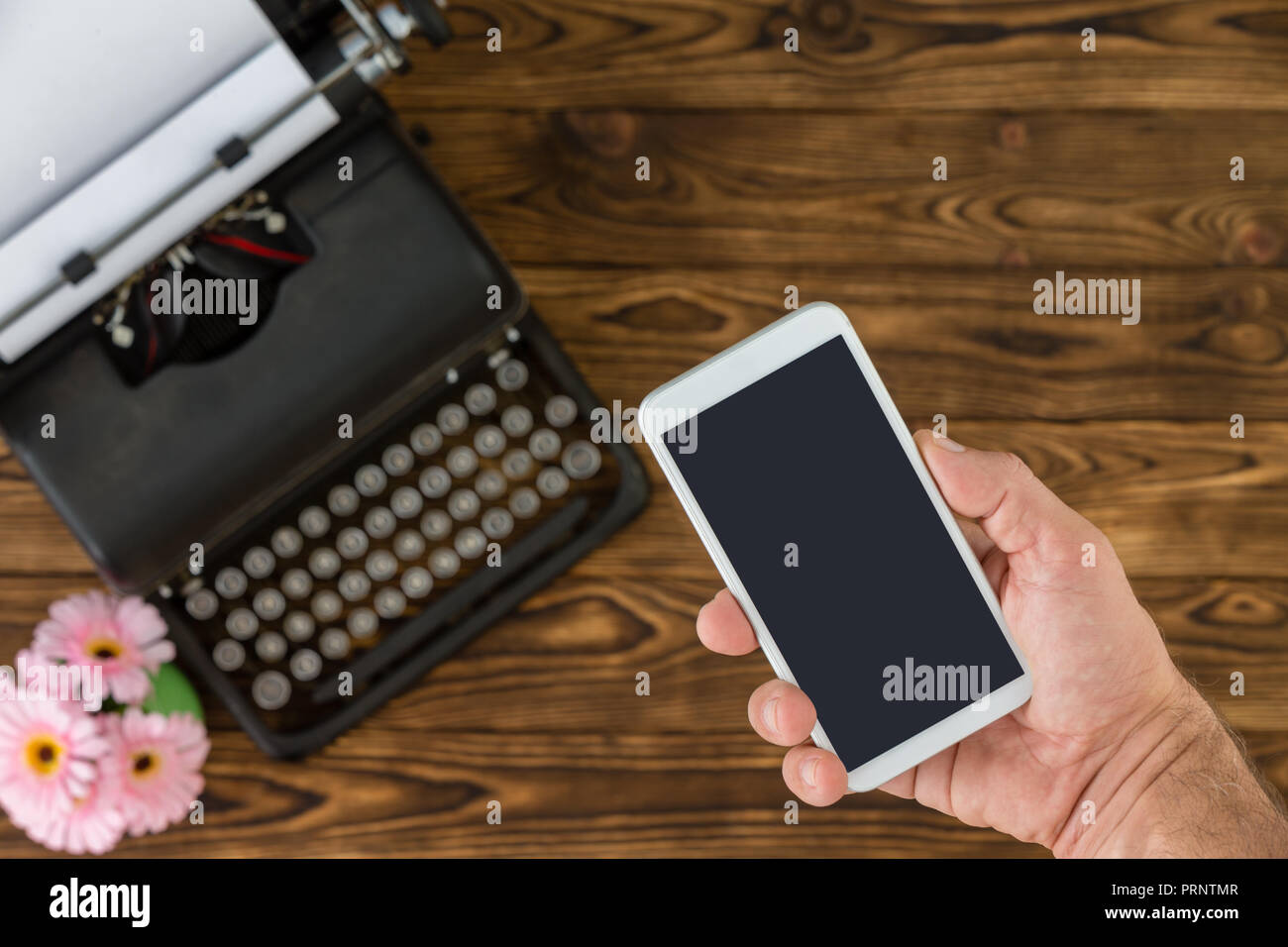 Nicht identifizierbarer Mann mit weissen smart phone neben Black Metal vintage Schreibmaschine und Kleine rosa Blumen Stockfoto