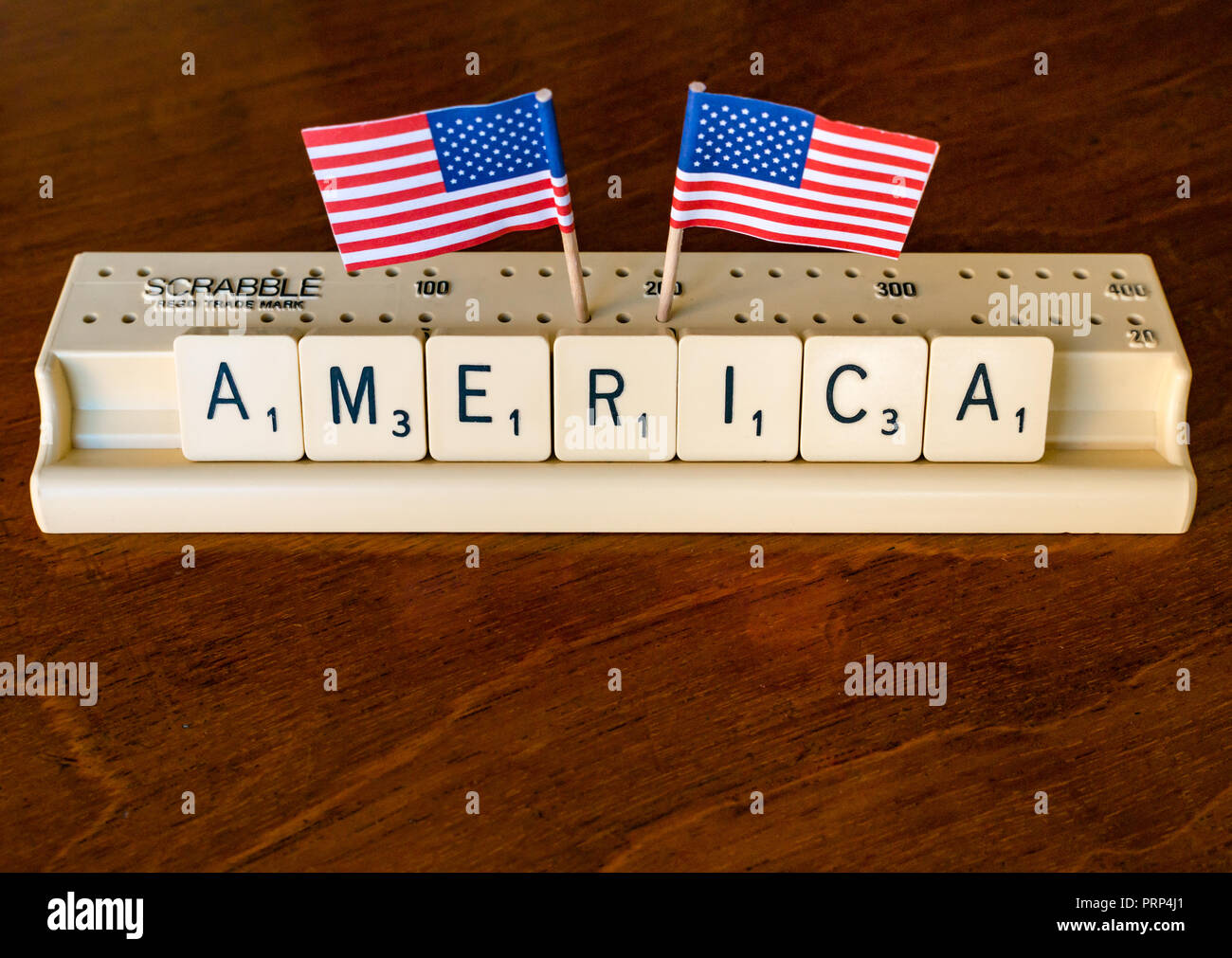 Scrabble Buchstaben Rechtschreibung Amerika in Scrabble Fach mit amerikanischen Stars and Stripes Flaggen auf dunklem Mahagoni Hintergrund Stockfoto