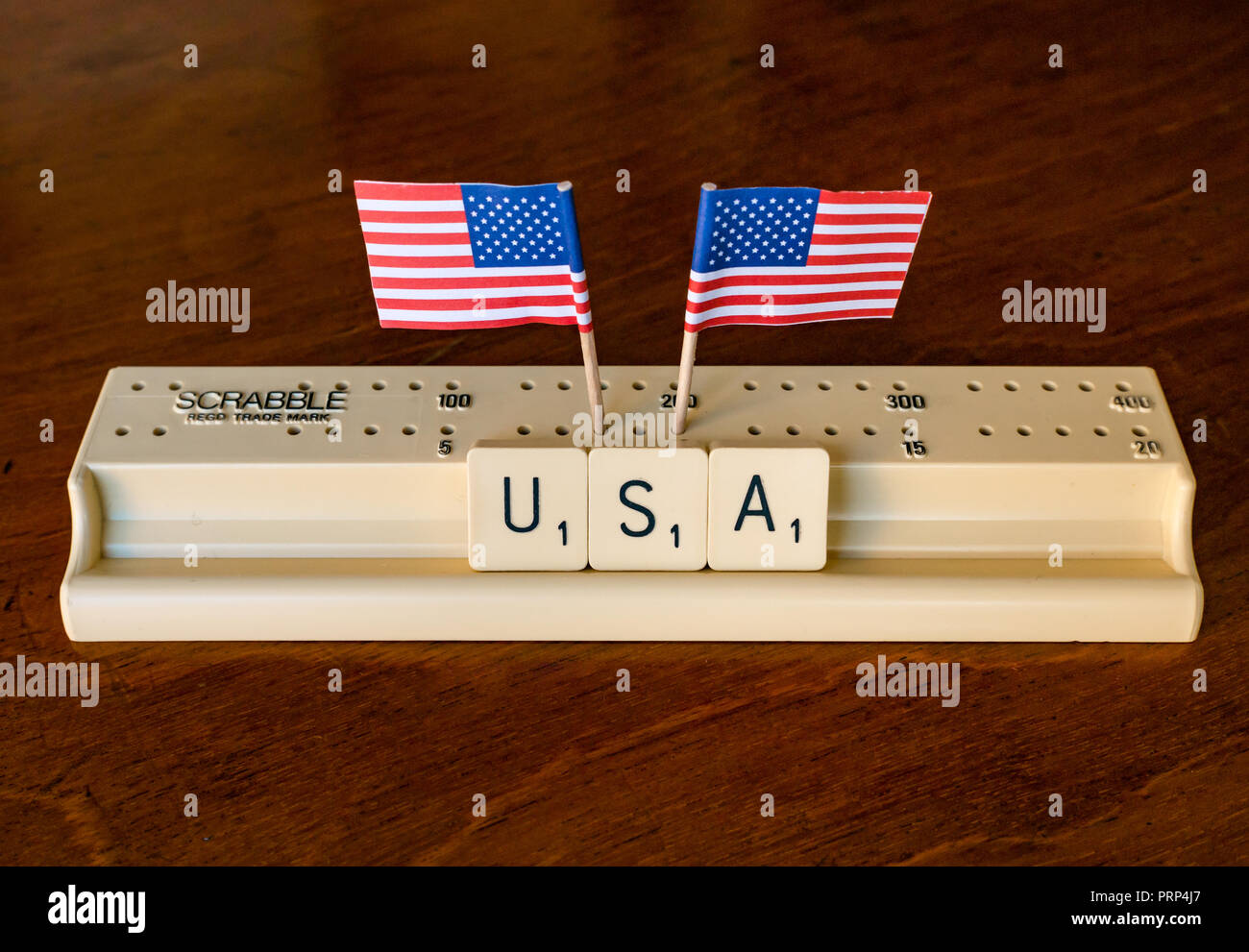 Scrabble Buchstaben Rechtschreibung USA in Scrabble Fach mit amerikanischen Stars and Stripes Flaggen auf dunklem Mahagoni Hintergrund Stockfoto