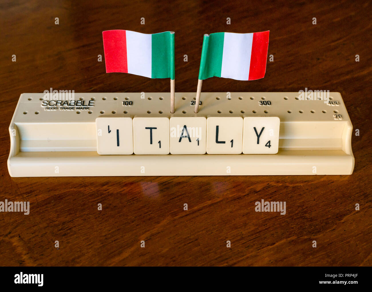 Scrabble Buchstaben Rechtschreibung Italien in Scrabble Fach mit italienischen Fahnen auf dunklem Mahagoni Hintergrund Stockfoto