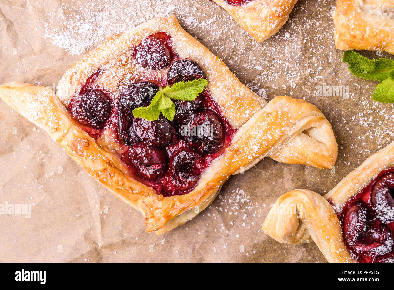 Hausgemachte Blätterteig mit Kirsche. Süß lecker Nachtisch. Mit Minze dekoriert. Auf Pergamentpapier. Stockfoto