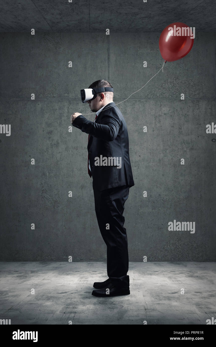 Unternehmer stehen mit VR-Headset auf Betonboden und halten roten Ballon in der Hand Stockfoto