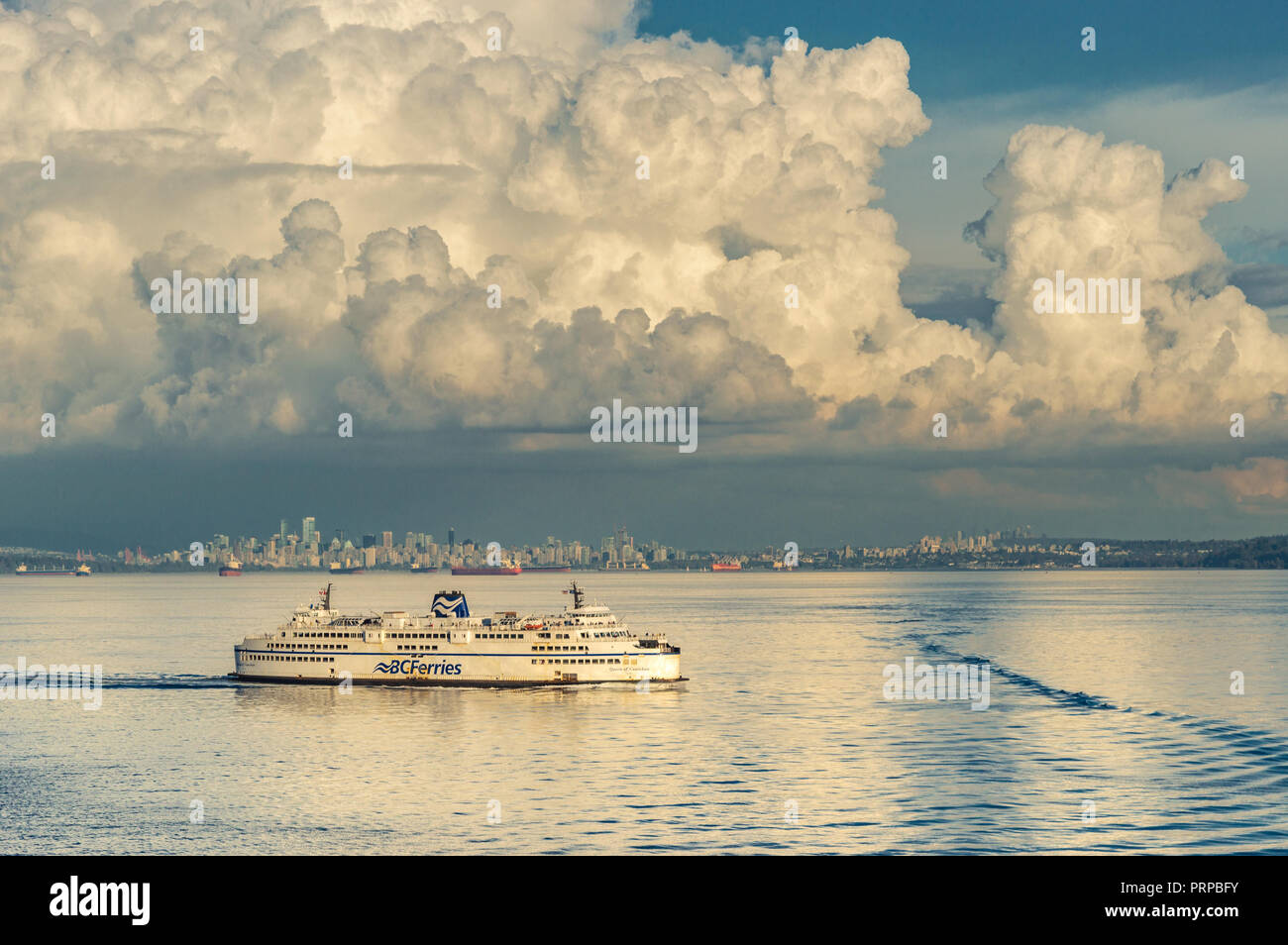 BC Ferries Fähre Königin der Cowichan Segel außerhalb der English Bay, in warmen Nachmittag Licht, Straße von Georgia, British Columbia, Kanada. Downtown Vancouver mit einem großen Cumulus cloud Overhead im Hintergrund. Stockfoto