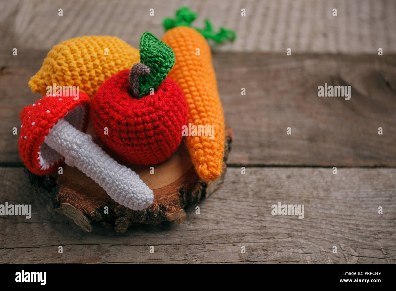Set aus Gewirken Spielzeug Zitrone, Karotte, Apfel, amanita auf Holz- Hintergrund. Früher taktile Entwicklung der Kinder, Handwerk Spielzeug, vegetarisches Menü Konzept, Stockfoto