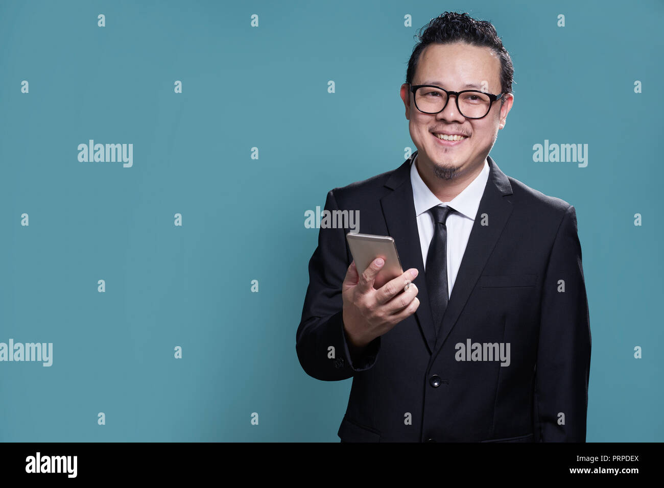 Portrait von Lächeln asiatische Geschäftsmann in Anzug und mit Smartphone. auf hellblauem Hintergrund isoliert. Stockfoto