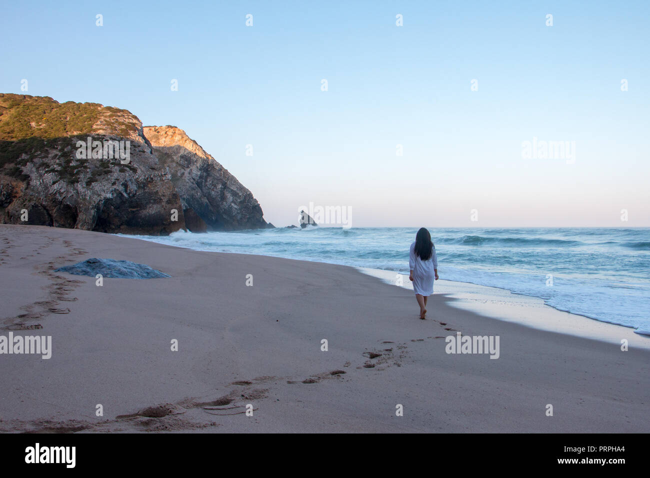 Frau, die zu Fuß auf einem schönen leeren Strand während der Sunrise und trug eine Nacht Kleid Stockfoto