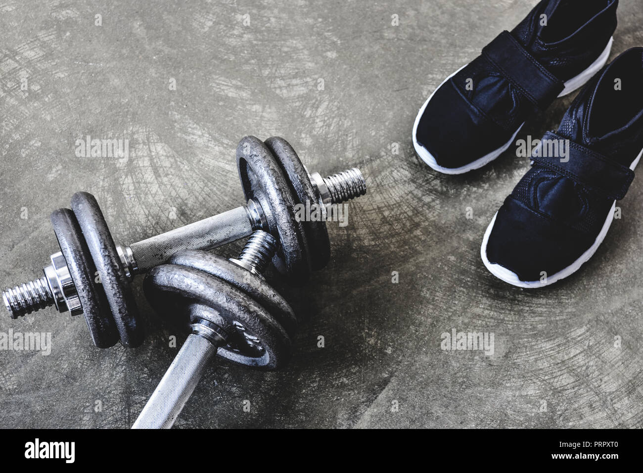 Nahaufnahme der Kompakthanteln mit Sneakers auf Betonoberfläche Stockfoto