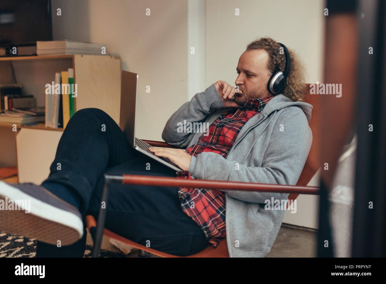 Mann in Casuals entspannen Sie sich auf einem Liegestuhl an seinem Laptop und Denken. Programmierer über eine neue Software Entwicklung arbeiten. Stockfoto