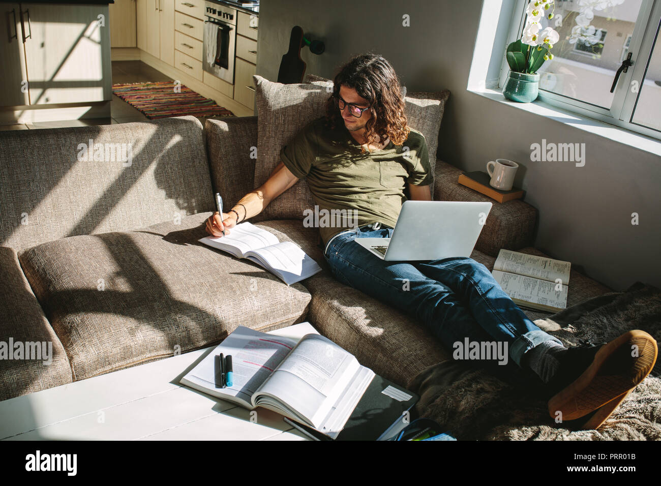 Student studieren für Prüfungen zu Hause bequem auf der Couch sitzen. Junger Mann mit Laptop zusammen mit Büchern zu studieren. Stockfoto