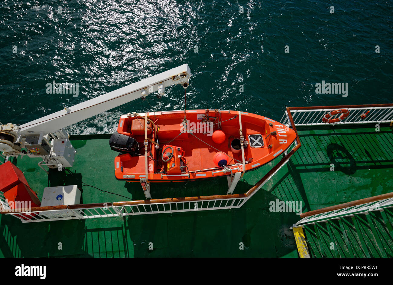 Kleine orangene Boot mit einem Außenbordmotor zu einem schwingenden Gantry auf eine Fähre verbunden. Für den Mann über Bord. Stockfoto