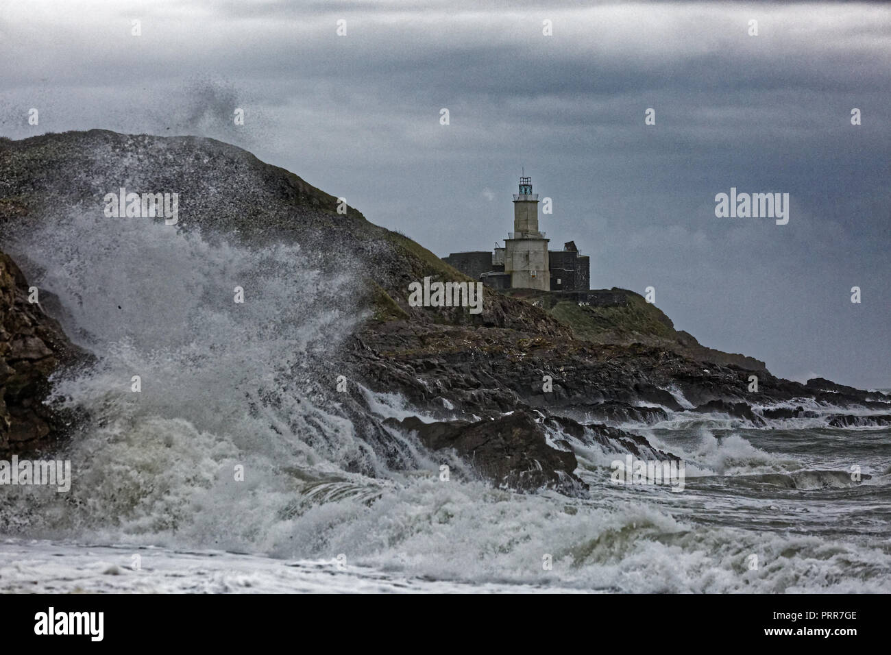 Wellen gegen die Felsen durch Mumbles Leuchtturm in Armband Bay, Swansea, Wales, Großbritannien Stockfoto