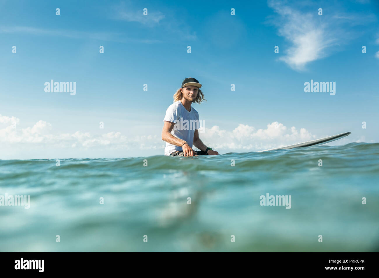 Selektiver Fokus der junge männliche Surfer Surfen im Meer am Sandstrand von Nusa Dua, Bali, Indonesien sitzen Stockfoto