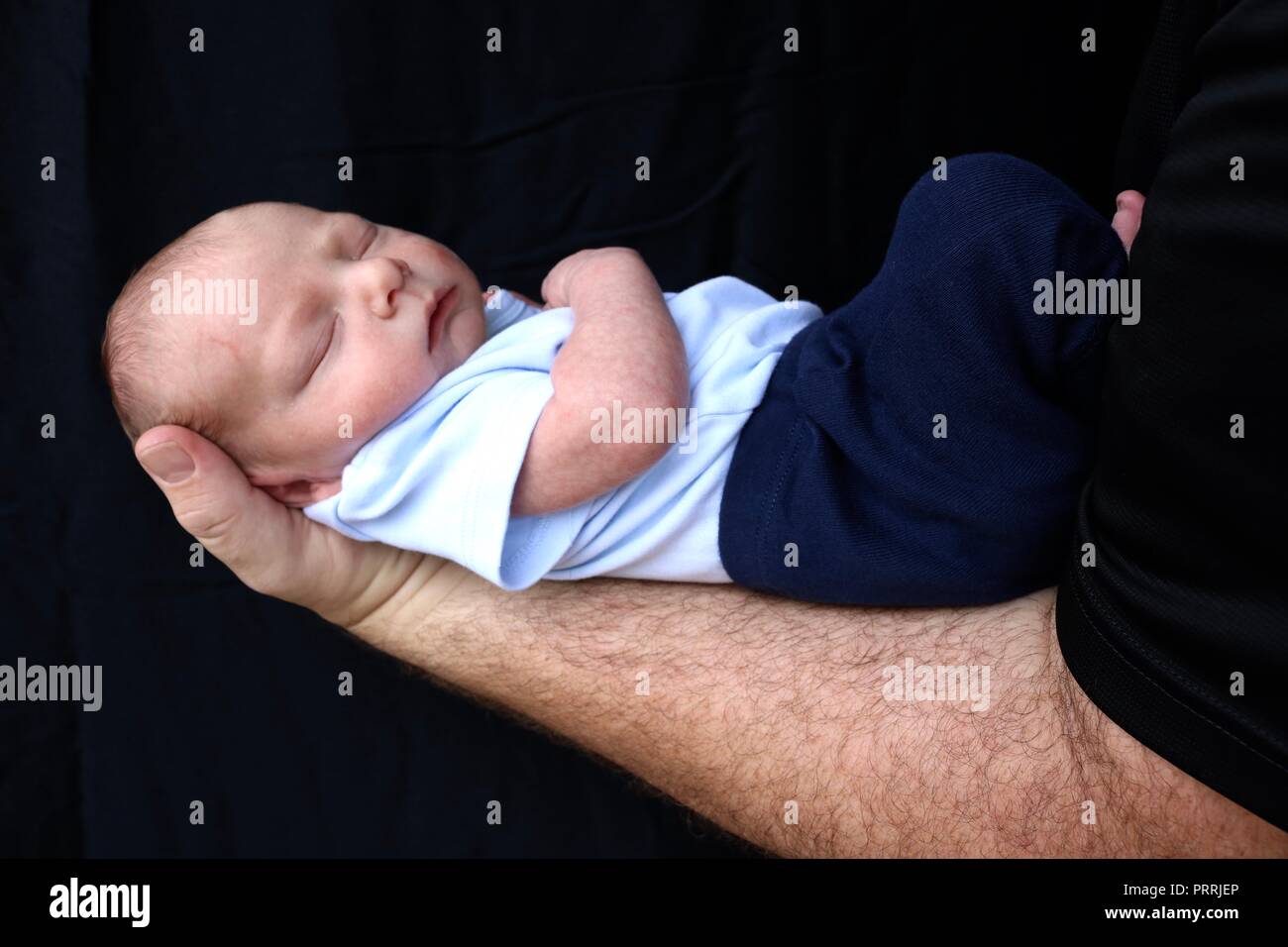 Neugeborene schlafen auf dem Arm seines Vaters vor einem schwarzen Hintergrund Stockfoto