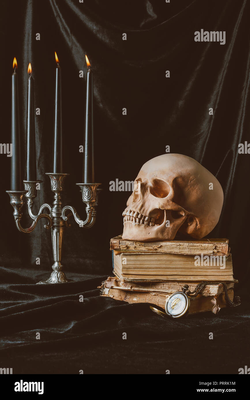 Schwarz halloween Kerzen, Schädel und alte Bücher auf schwarzem Stoff Stockfoto