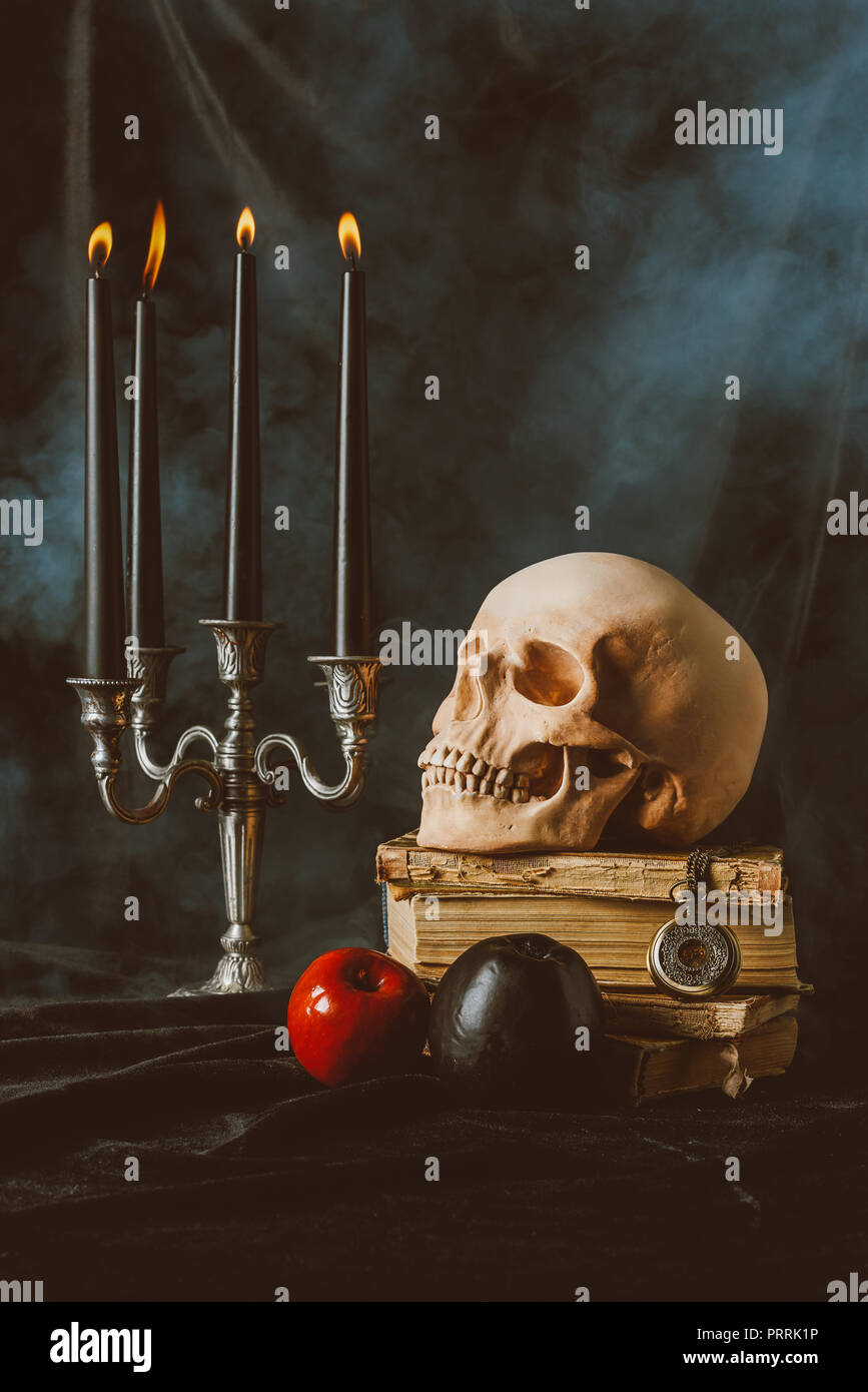 Armleuchter, Halloween Totenkopf, alte Bücher mit schwarzen und roten Äpfeln auf schwarzem Stoff mit Rauch Stockfoto