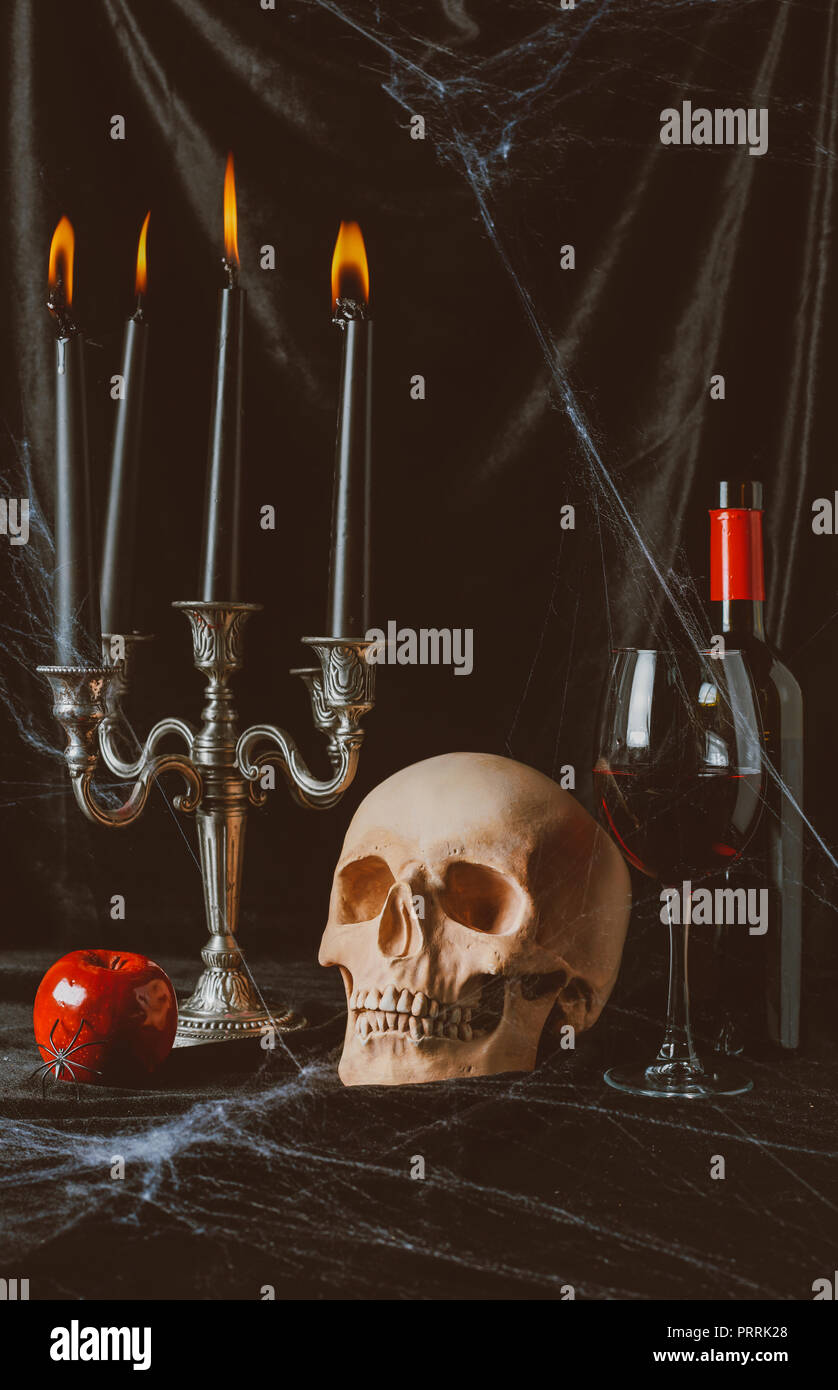 Halloween Totenkopf, Apple, Rotwein und Kandelaber mit Kerzen auf schwarzem Stoff mit Spinnennetz Stockfoto
