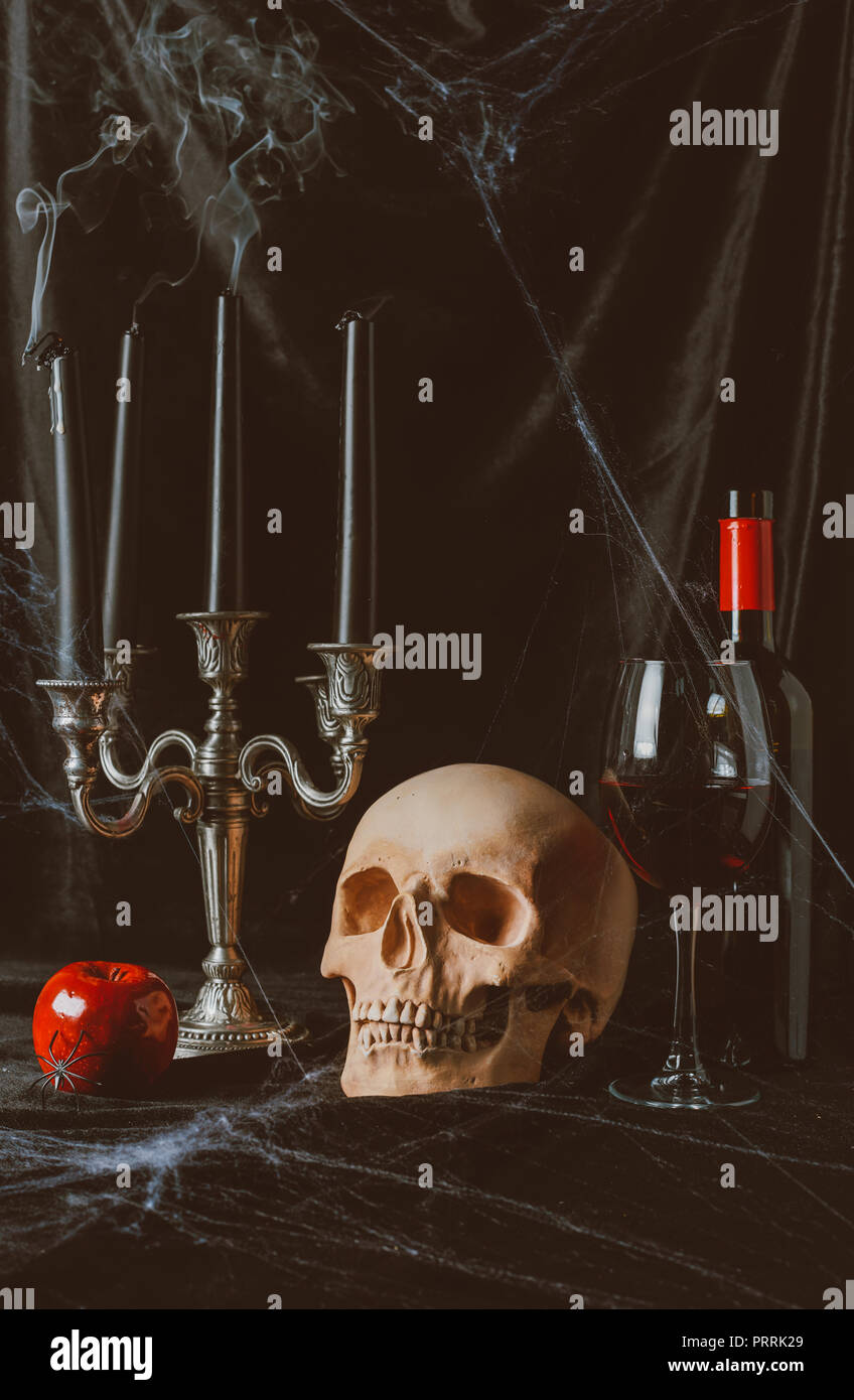 Schädel, Apple, Rotwein und Kandelaber mit rauchigen Kerzen auf schwarzem Stoff mit Spinnennetz Stockfoto