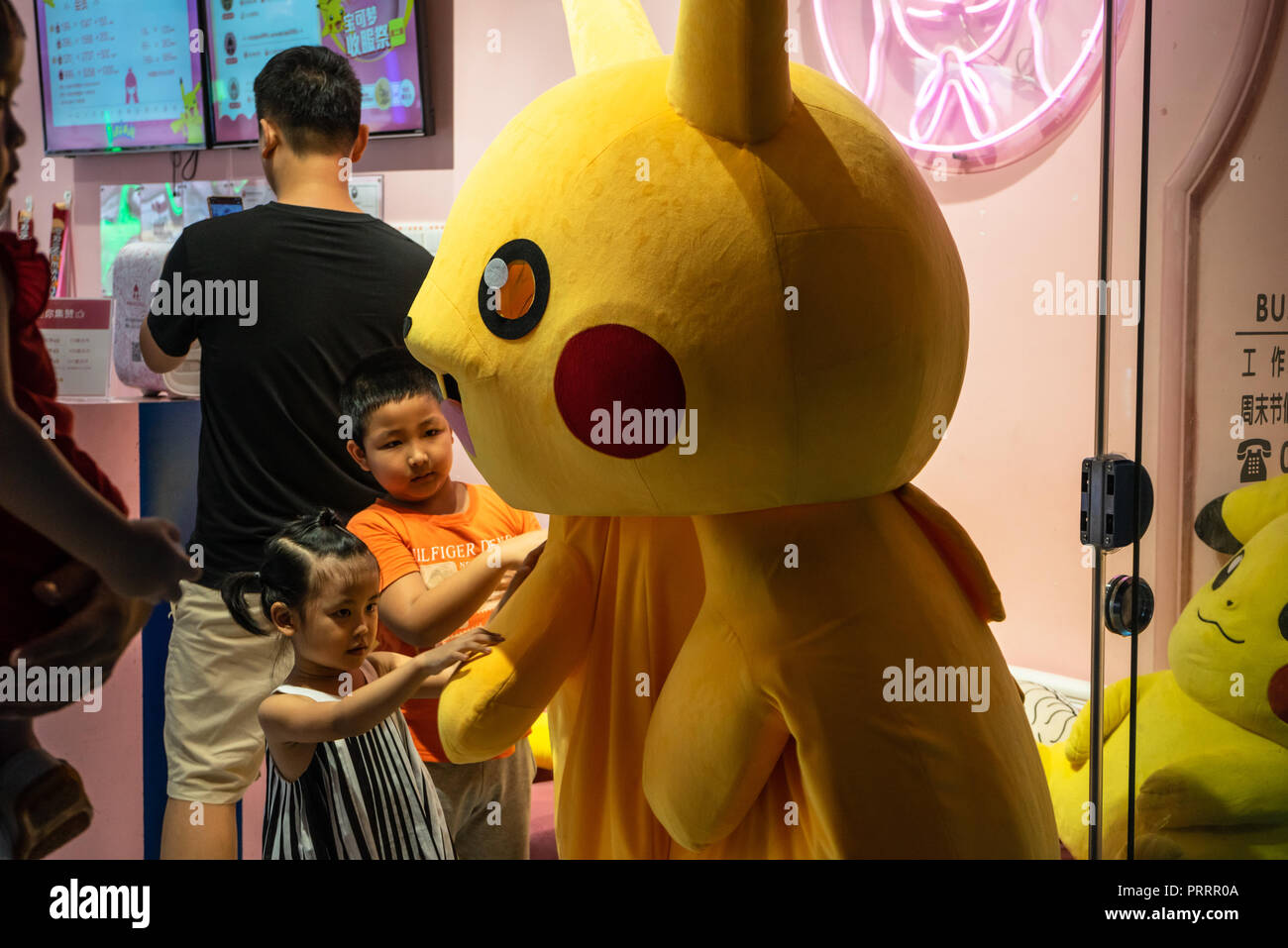 Neugierige Kinder reiben Arme von Pikachu Maskottchen in Pikachu Kostüm Stockfoto
