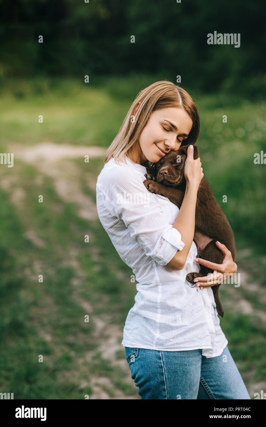 Seitenansicht der junge lächelnde Frau umarmen süße Labrador Welpen in den Händen Stockfoto