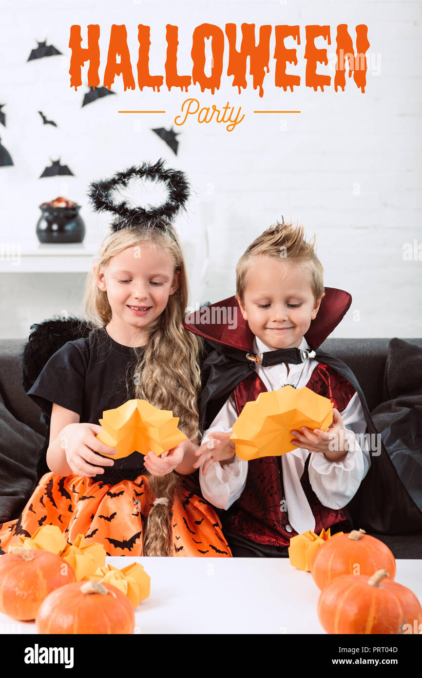 Portrait von kleinen Geschwister in Halloween Kostüme sitzen auf einem Sofa am Tisch mit Kürbissen zu Hause mit 'halloween party'-Schriftzug Stockfoto