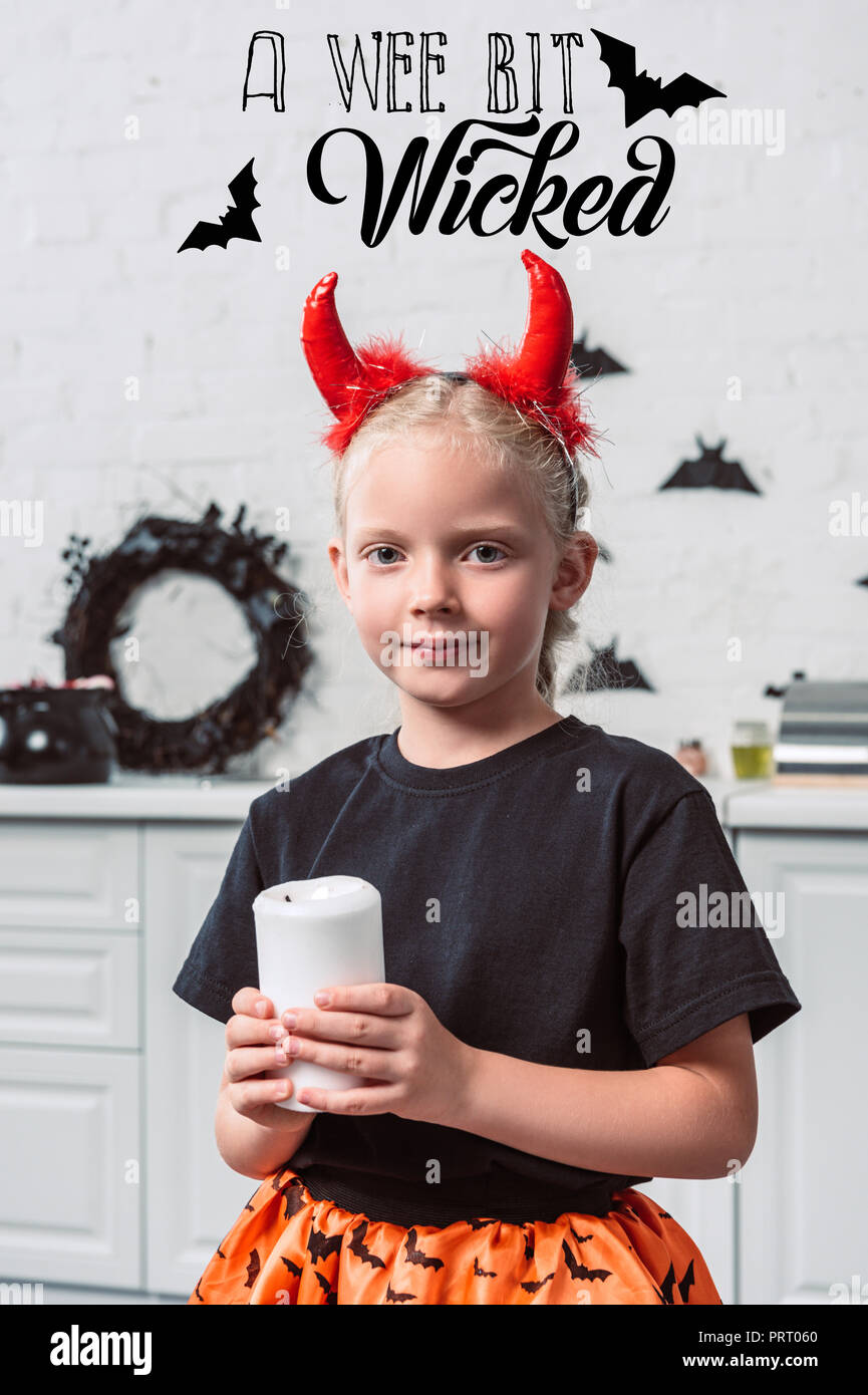 Portrait von kleines Kind mit roten Teufel Hörner mit Kerze in der Hand zu Hause, halloween Urlaub Konzept mit "ein bisschen böse' Schriftzug Stockfoto