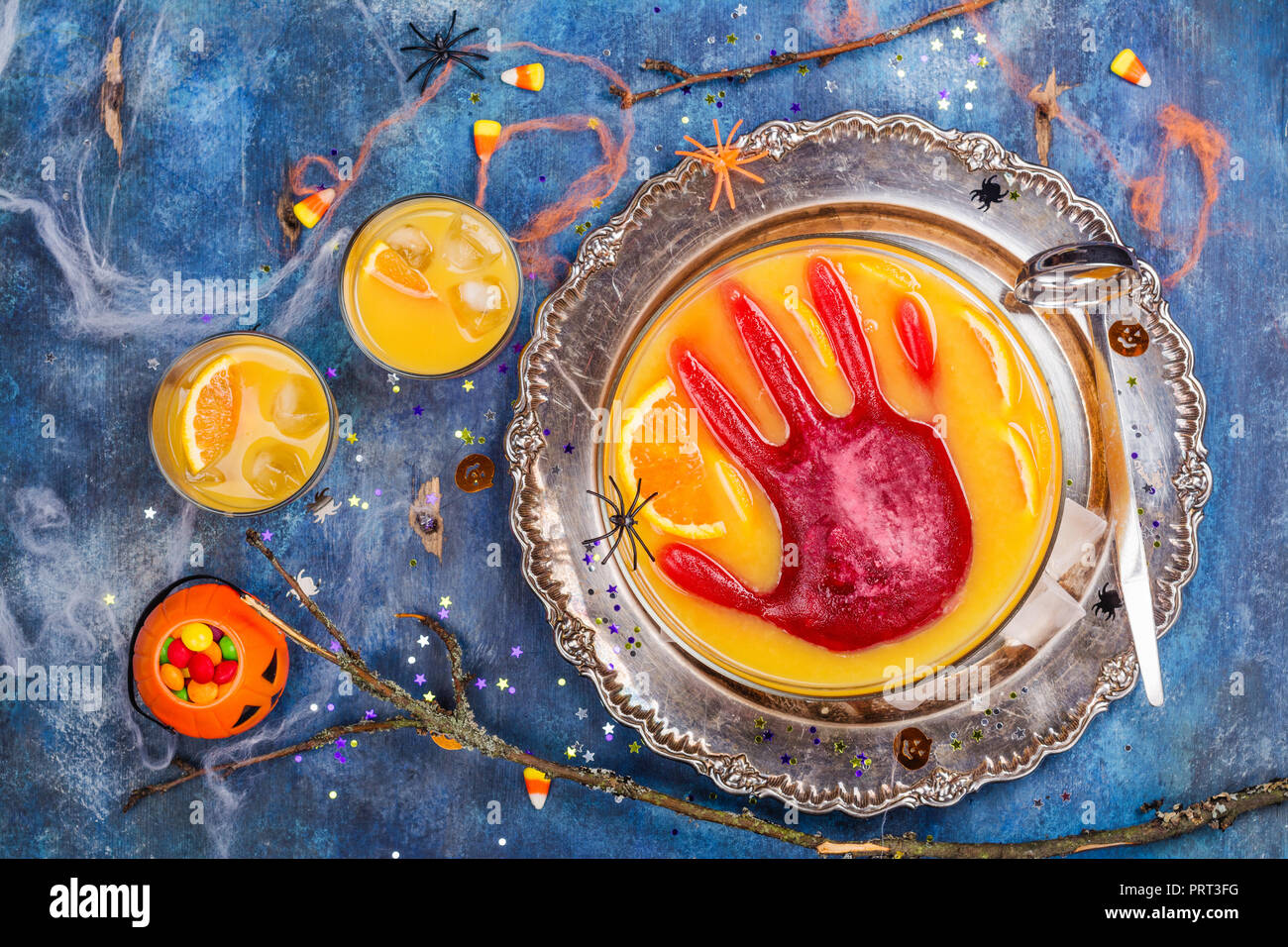 Ghoul orange Punch mit blutigen Eis Hand in eine Glasschüssel auf dunklen halloween Hintergrund Stockfoto