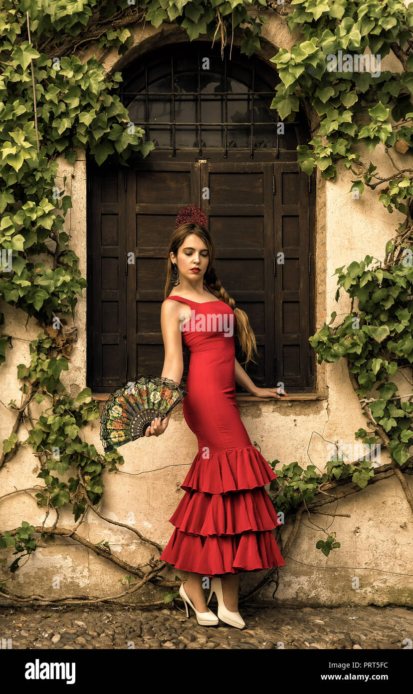 Spanische Frau im roten Kleid vor einem alten Fenster posieren. Stockfoto