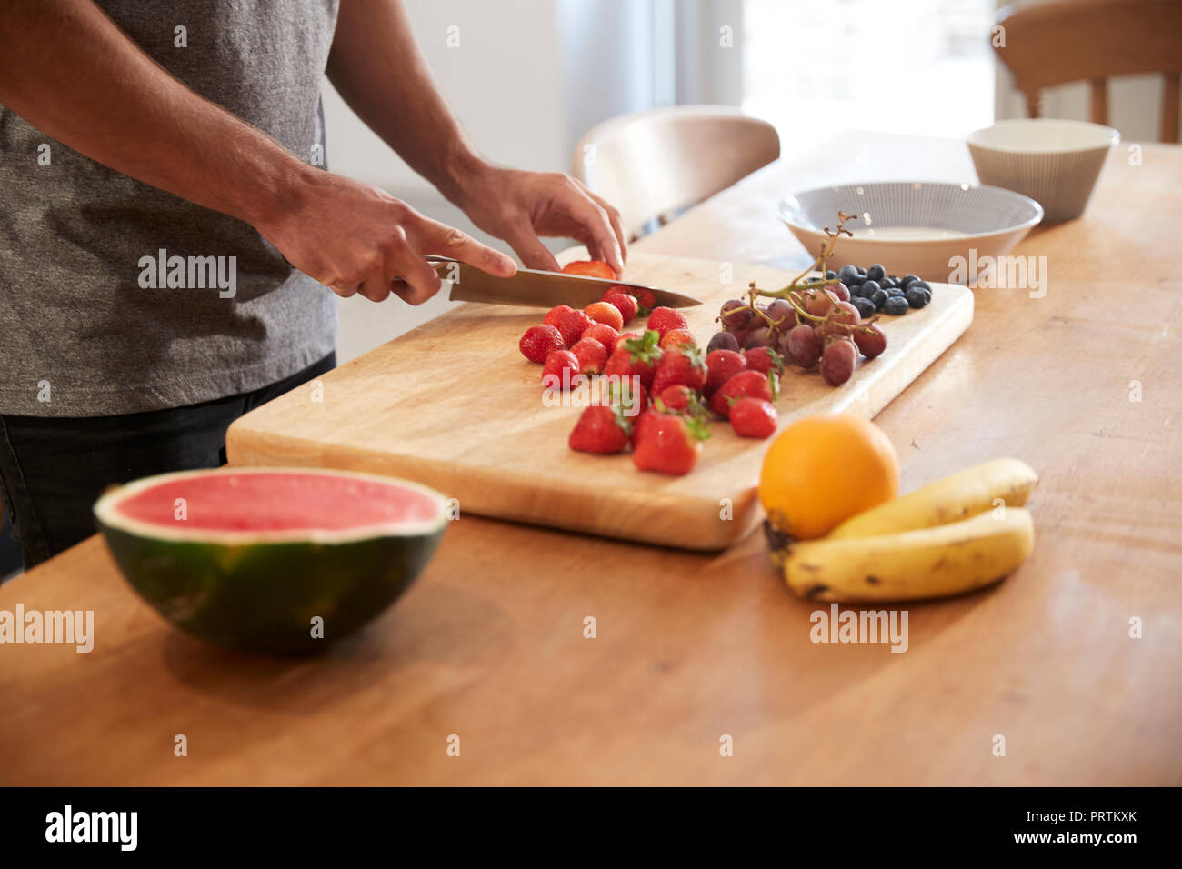 Junger Mann schneiden frisches Obst am Küchentisch, mittlerer Abschnitt Stockfoto