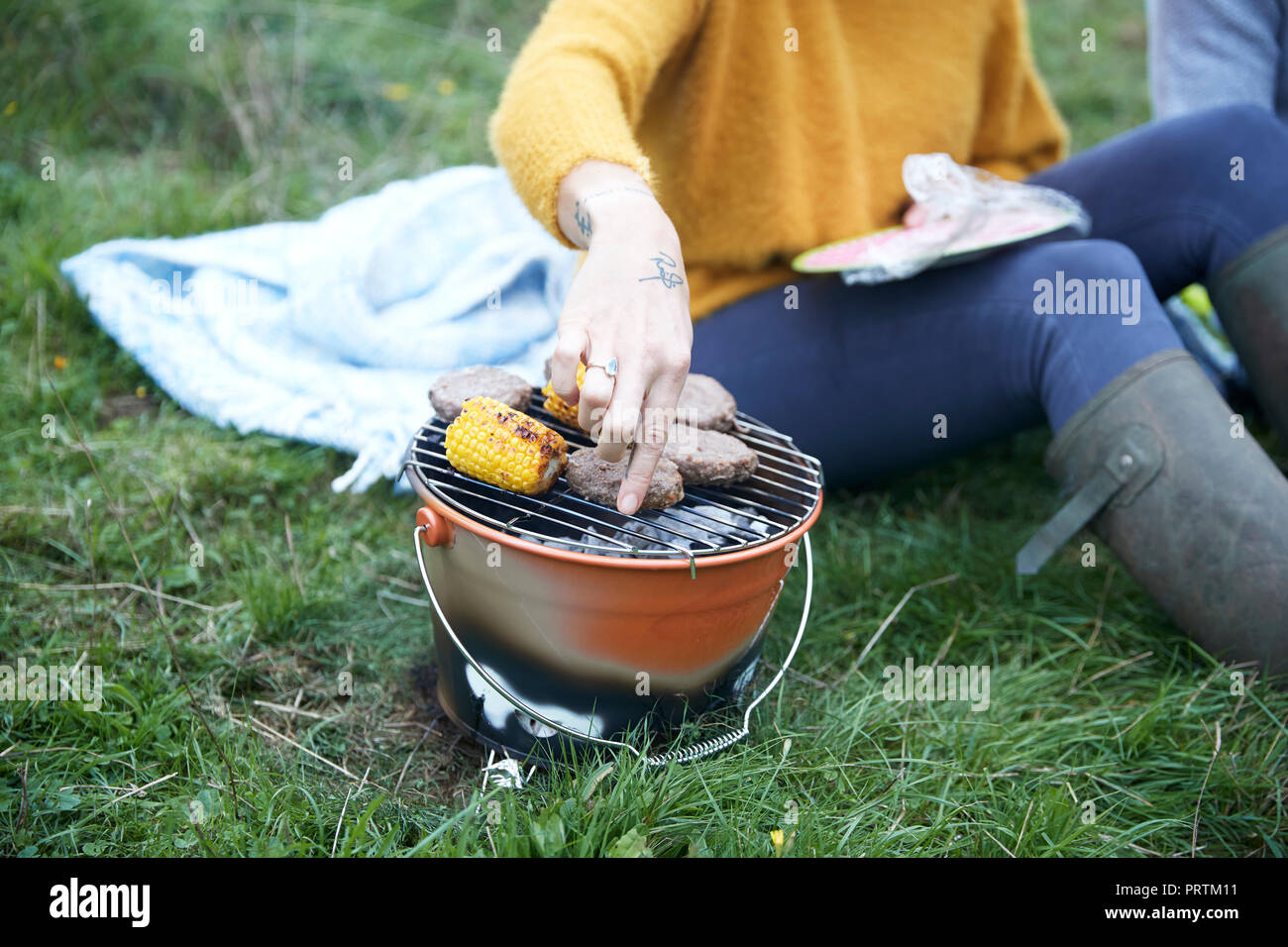 Frau und Freund sitzen im ländlichen Bereich Kochen auf Grill, 7/8 Stockfoto