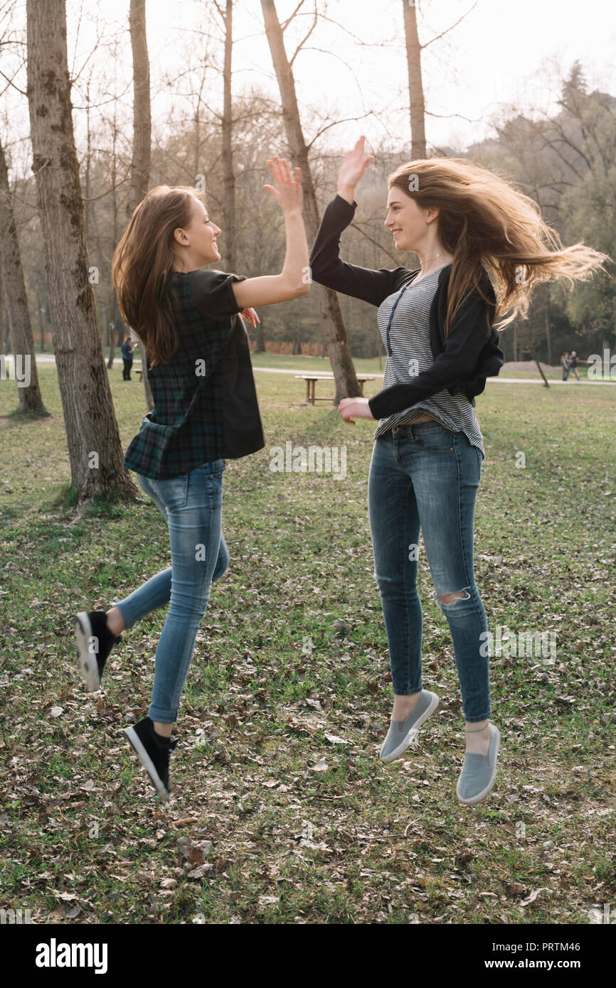 Freundinnen springen und dabei hoch fünf im Park Stockfoto