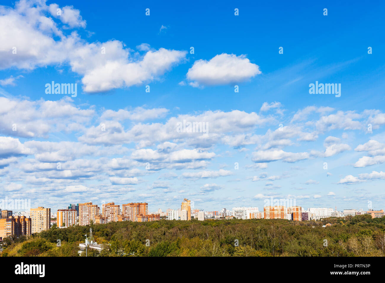 Viele weiße Wolken im blauen Himmel über Häuser und städtischen Park im sonnigen Herbsttag Stockfoto