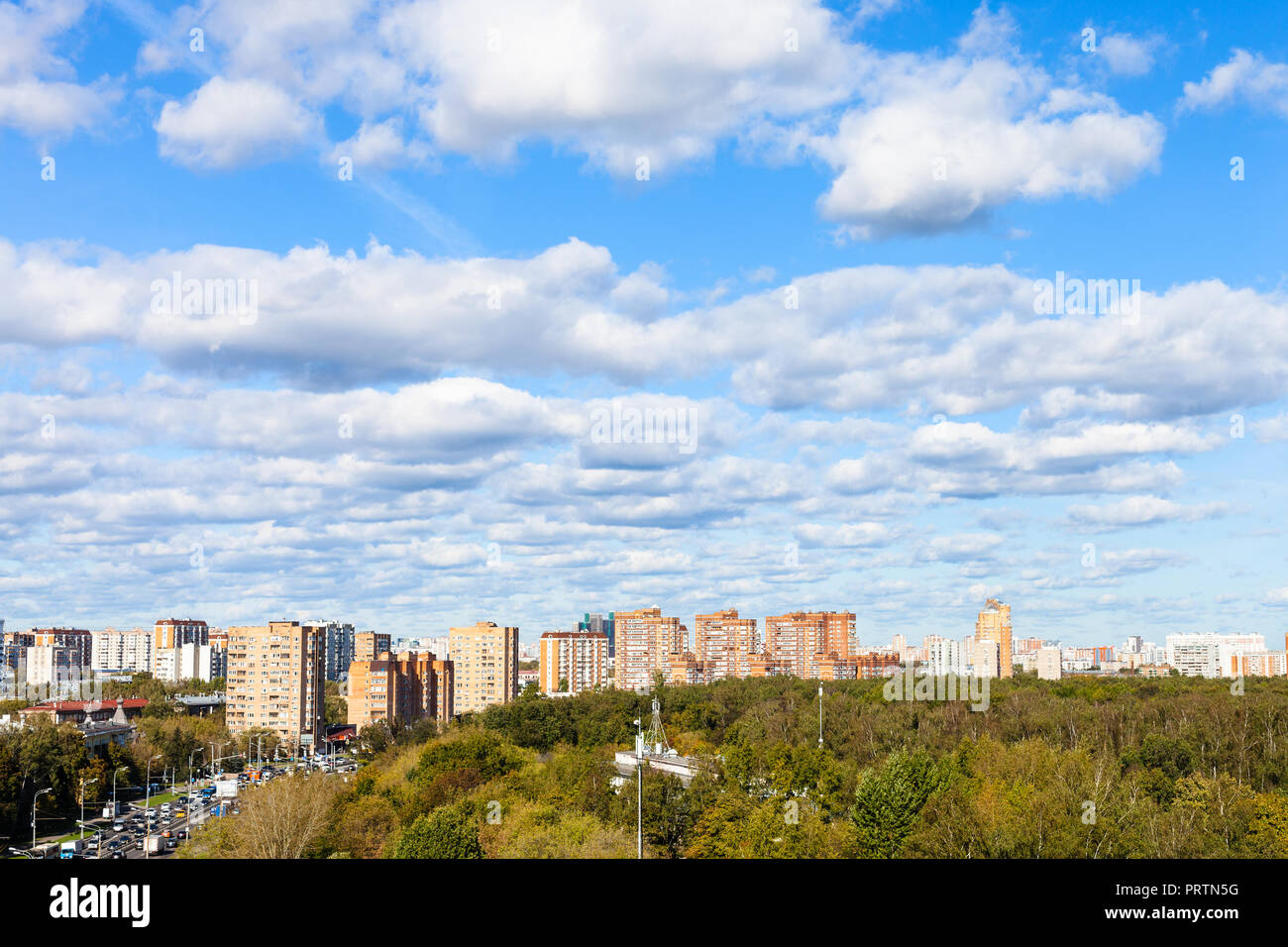Weiße Wolken im blauen Himmel über Straße und städtischen Park im sonnigen Herbsttag Stockfoto