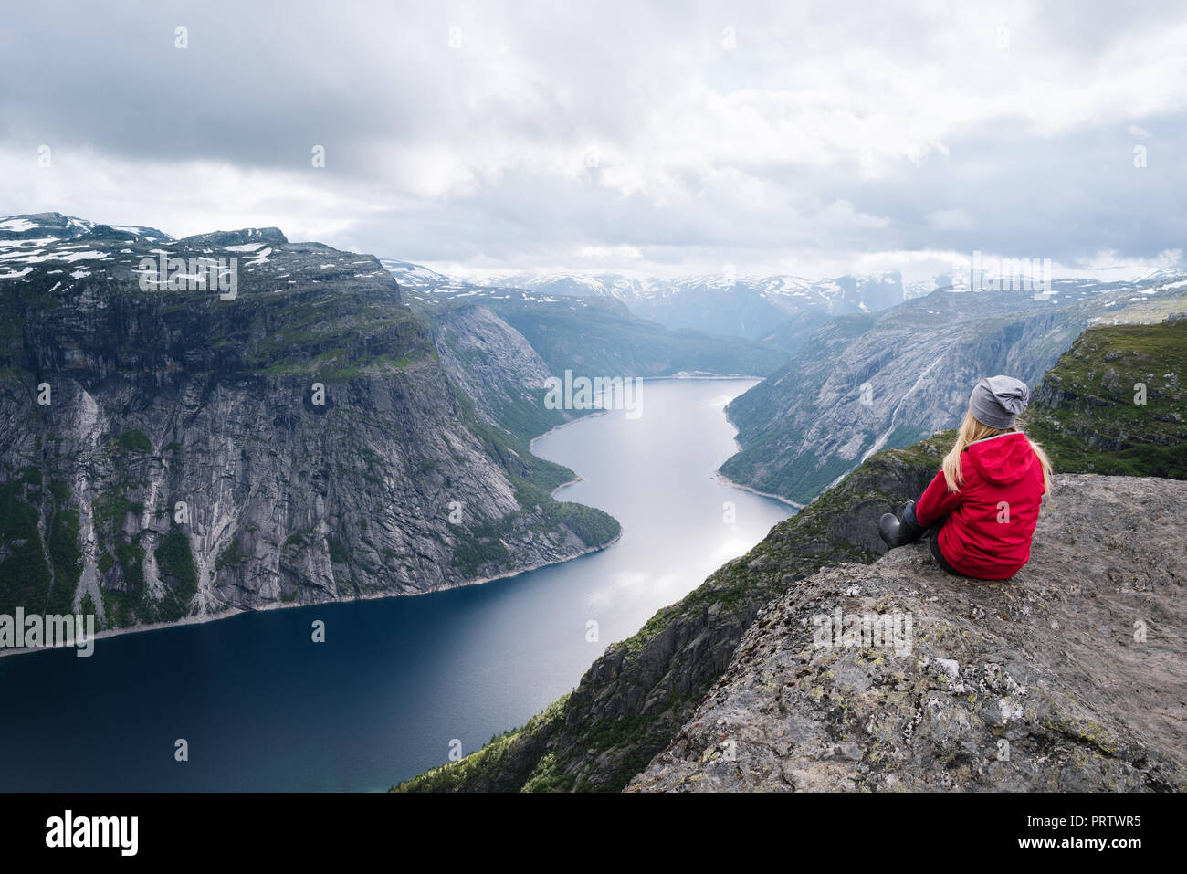 Majestic Trolltunga - eine von Norwegens spektakulärer Anblick. Mädchen in der roten Jacke sitzt auf Felsen und blickt auf Ringedalsvatnet See Stockfoto