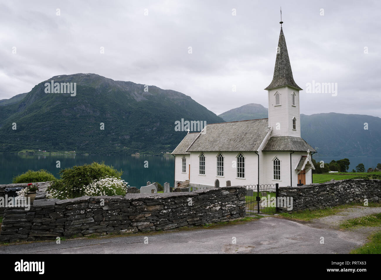 Weiß Holz- Norwegische Kirche - Nes kyrkje, Gemeinde Glanz, Norwegen. In der Nähe von Fjord Lusterfjord. Sommer bewölkt Landschaft Stockfoto