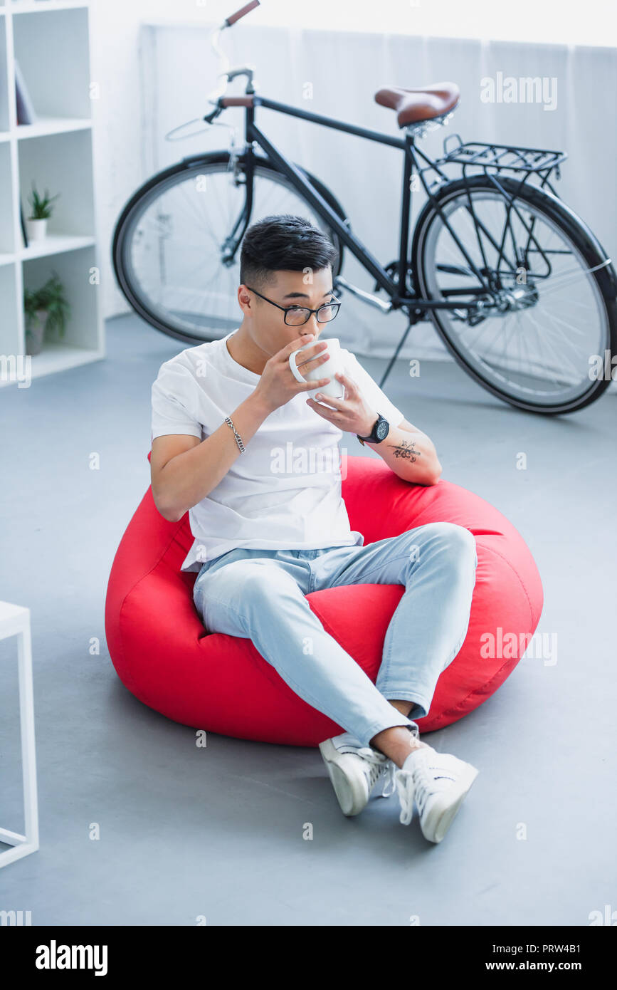 Hohe Betrachtungswinkel von Stattlichen asiatischer Mann auf Sitzsack und Tee trinken zu Hause sitzen Stockfoto
